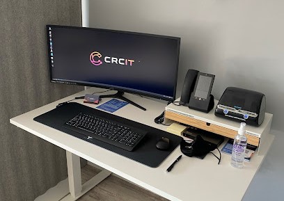 A clean and nicely setup CRCIT workstation on a sit stand desk with wide screen monitor displaying the CRCIT logo